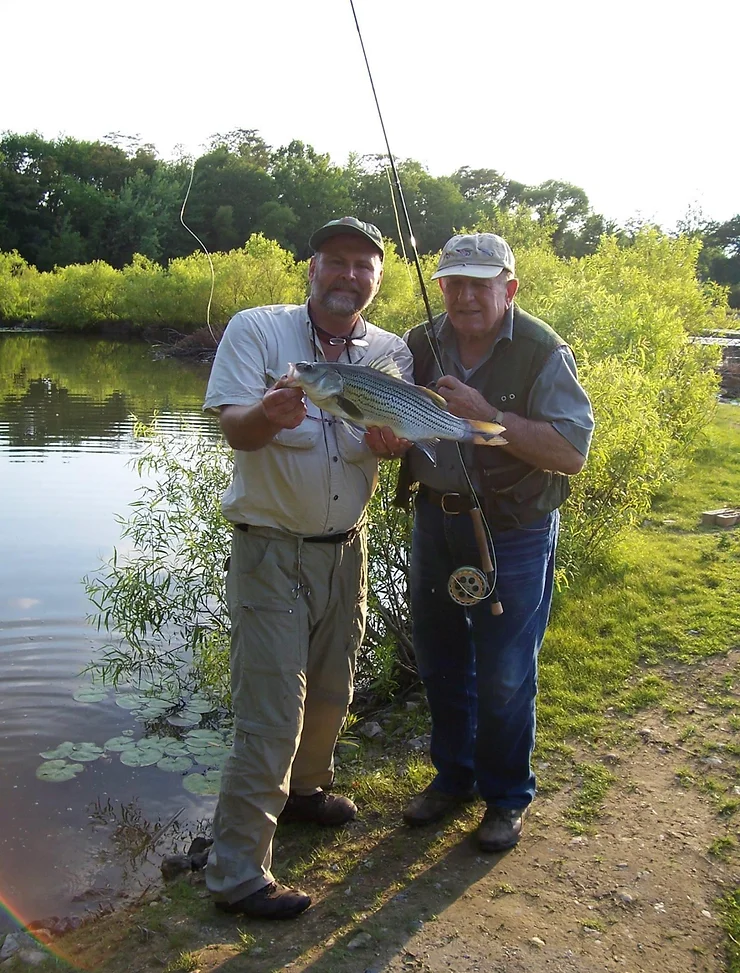 Ed Shenk enjoyed fly fishing clear up until his death in 2020. Here, Bill Skilton, left, hoists one of Shenk's last catches.