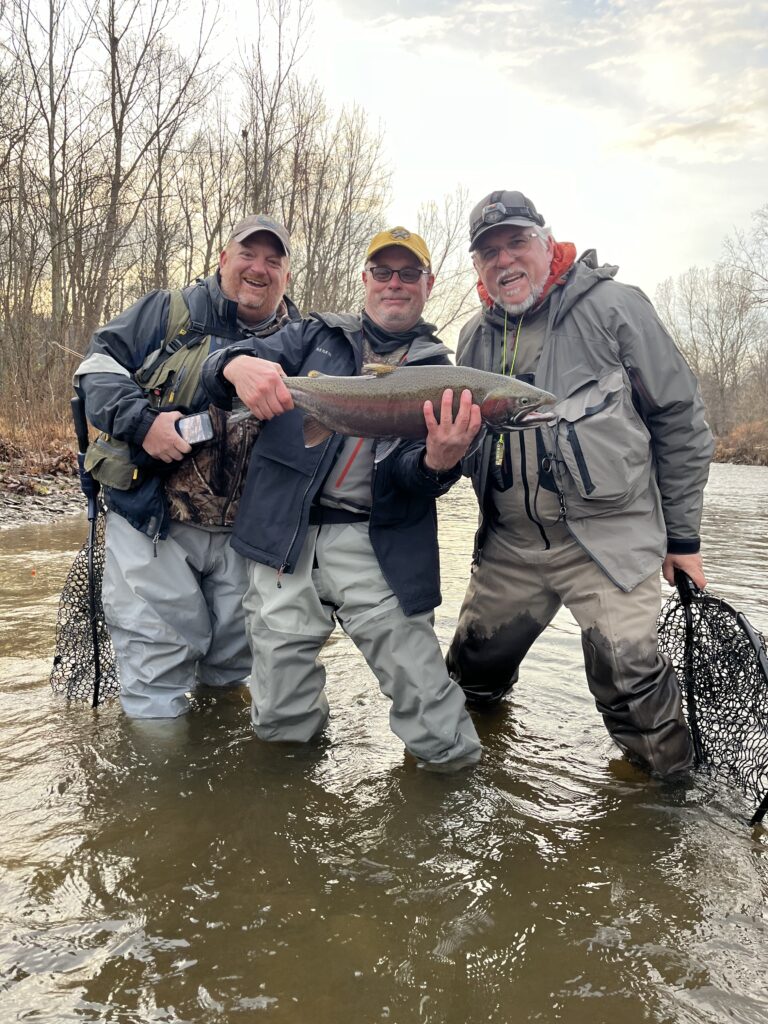 three guys with a fish on a stream