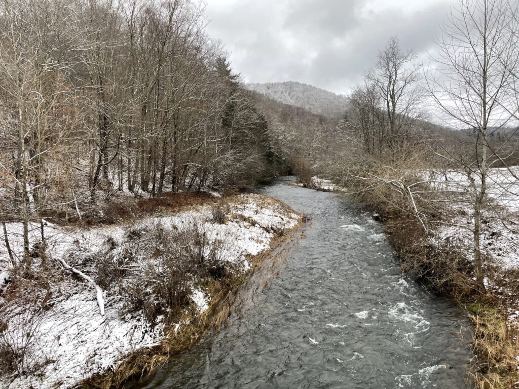 stream flowing through a meadow with snow