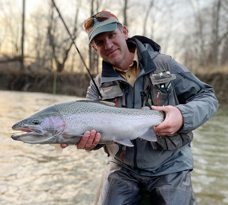 man holding steelhead in a stream