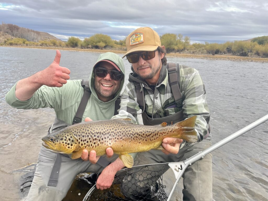two guys holding a trout in a river