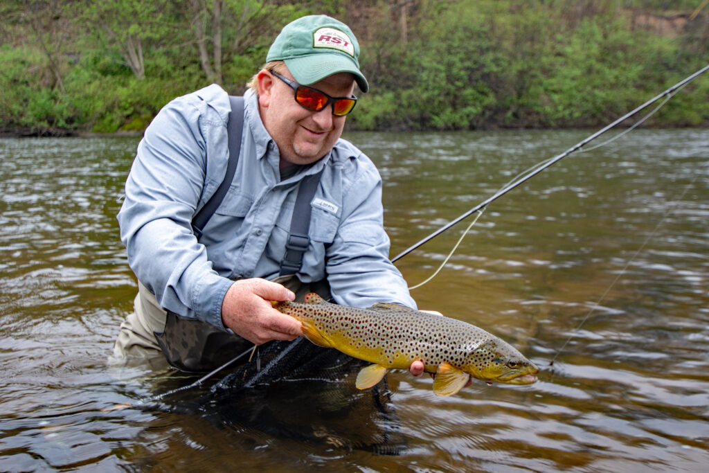 man holding brown trout in a river