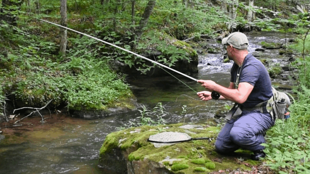 man fishing from a rock in a stream