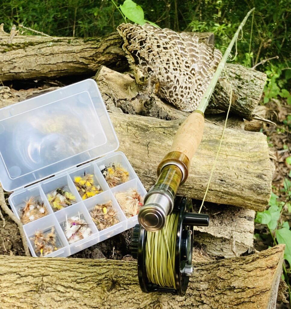 fly rod and fly box on a wood pile